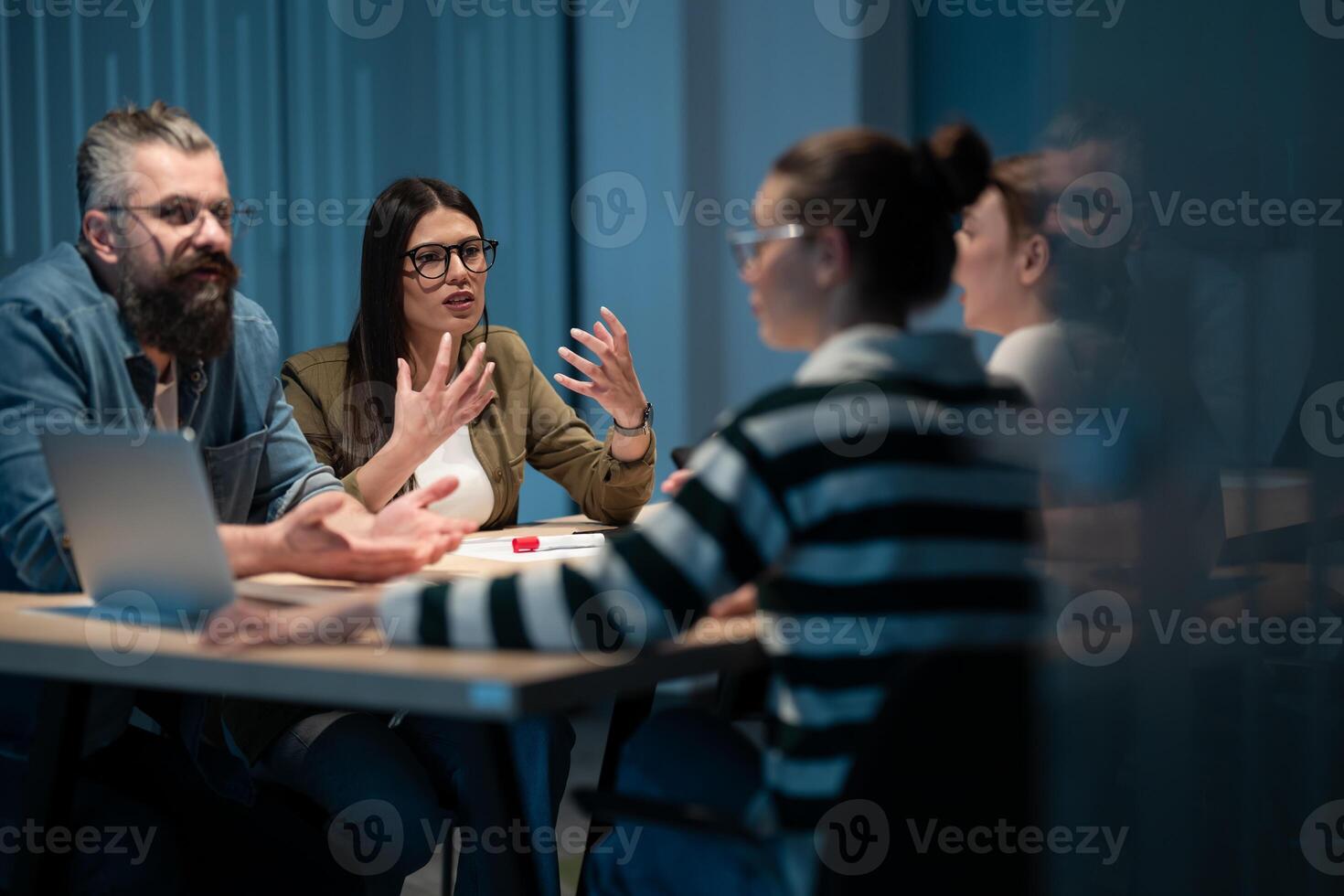 A diverse team of young professionals collaborates in a modern office conference room. Businesspeople discuss strategy, technology, and planning, using laptops to develop an innovative e-commerce photo