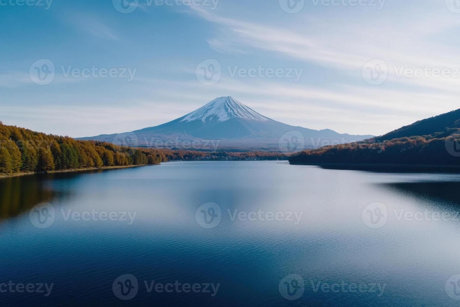 Snow-capped peak of mountain over serene lake, surrounded by autumnal trees in clear daylight photo