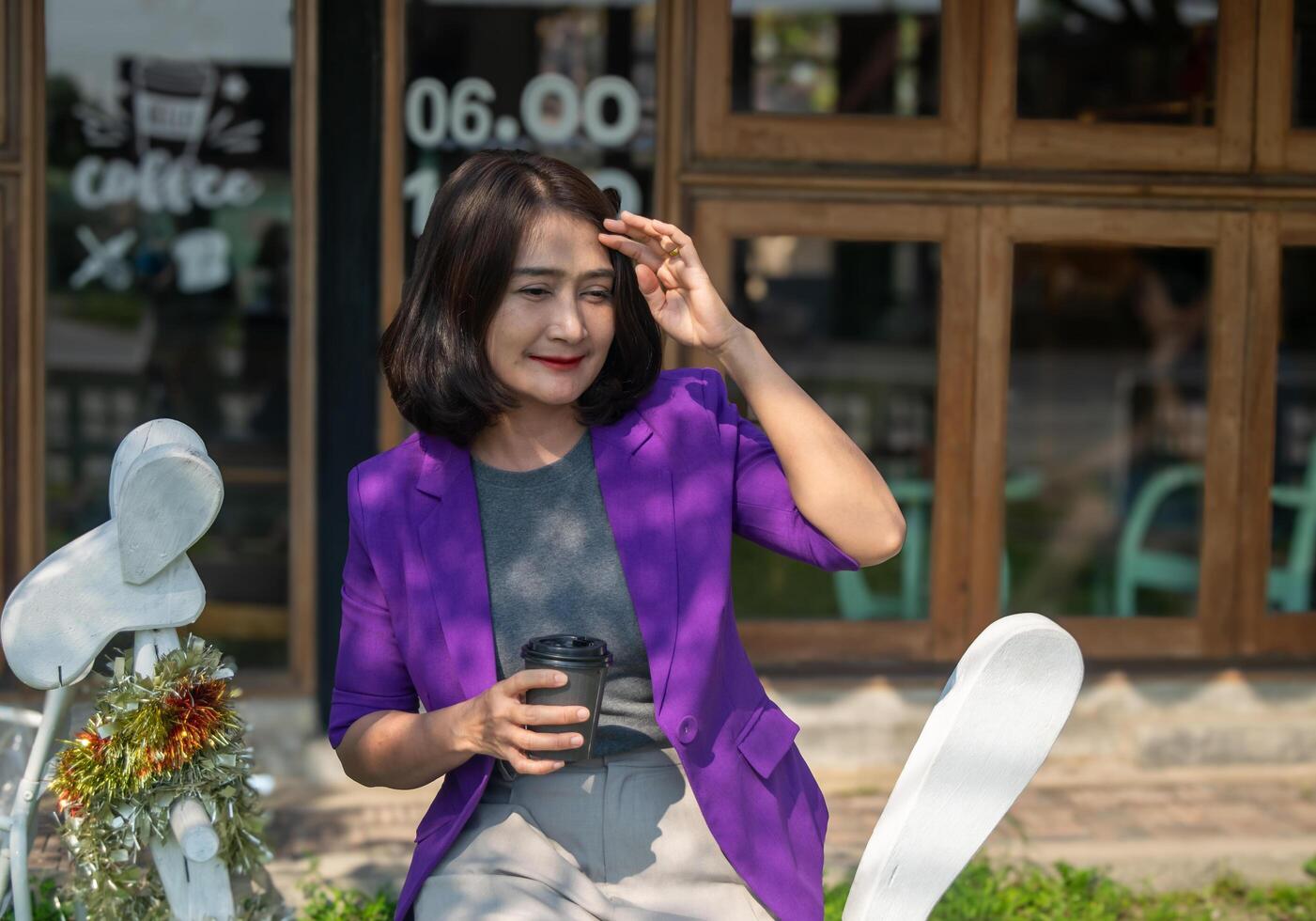 Asian woman sitting on bench hand holding a steaming cup of coffee outside cafe shop and smiling happy on vacation ,relaxing lifestyle concepts photo