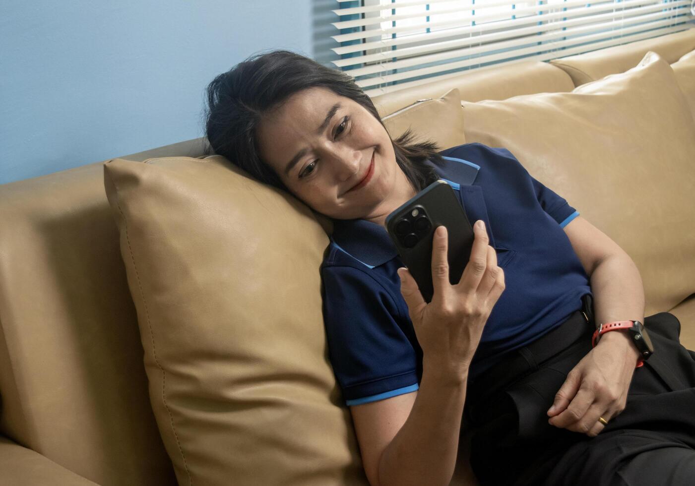 Asian woman lying down on sofa using mobile phone shopping online, watching social media network, relaxing lifestyles at home photo
