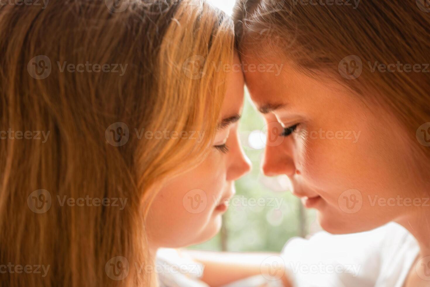 Sisters Foreheads Touching Indoor Closeup. Affectionate bond between two young sisters touching foreheads indoors, showcasing intimacy and love. photo
