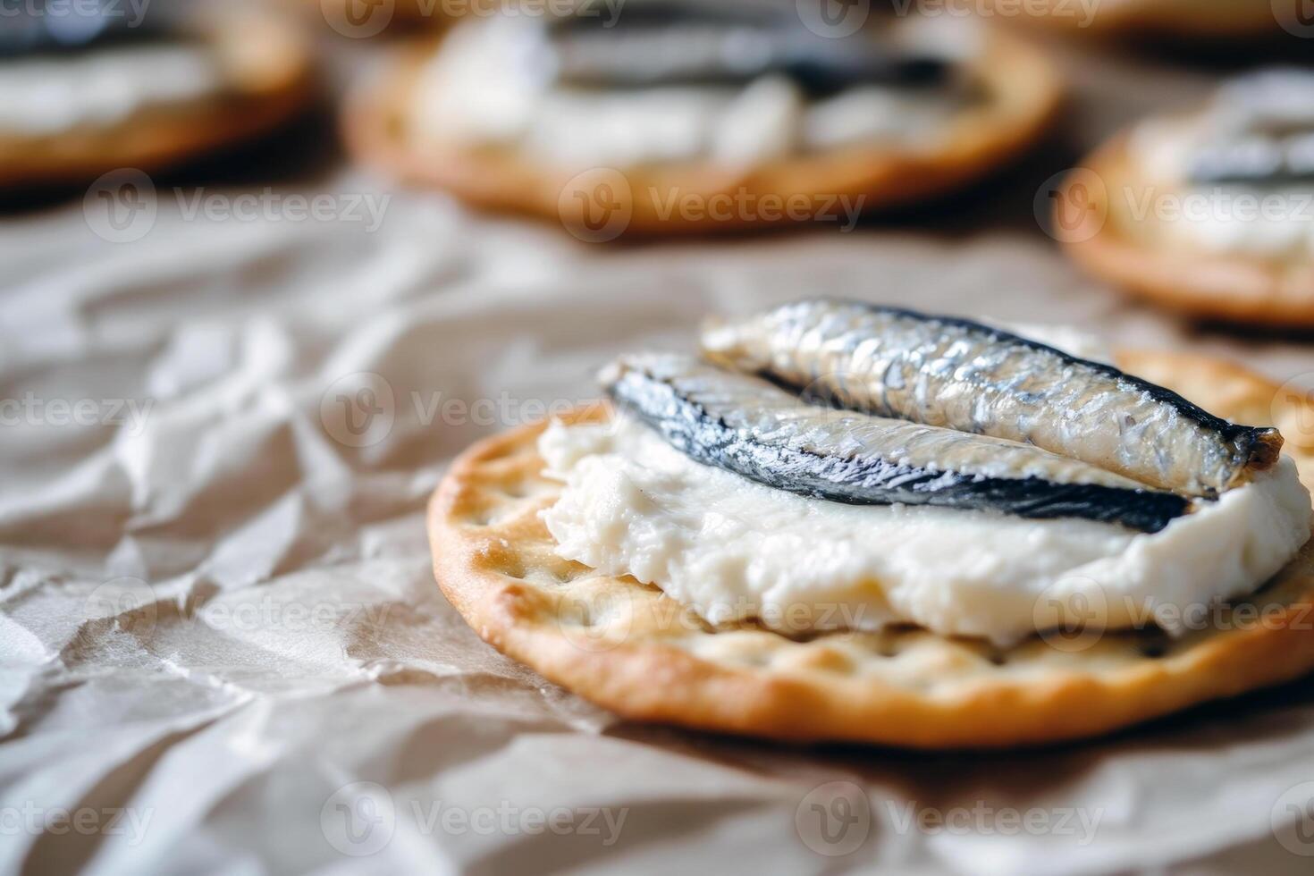 Sardine-topped crackers with cream cheese on brown paper surface photo