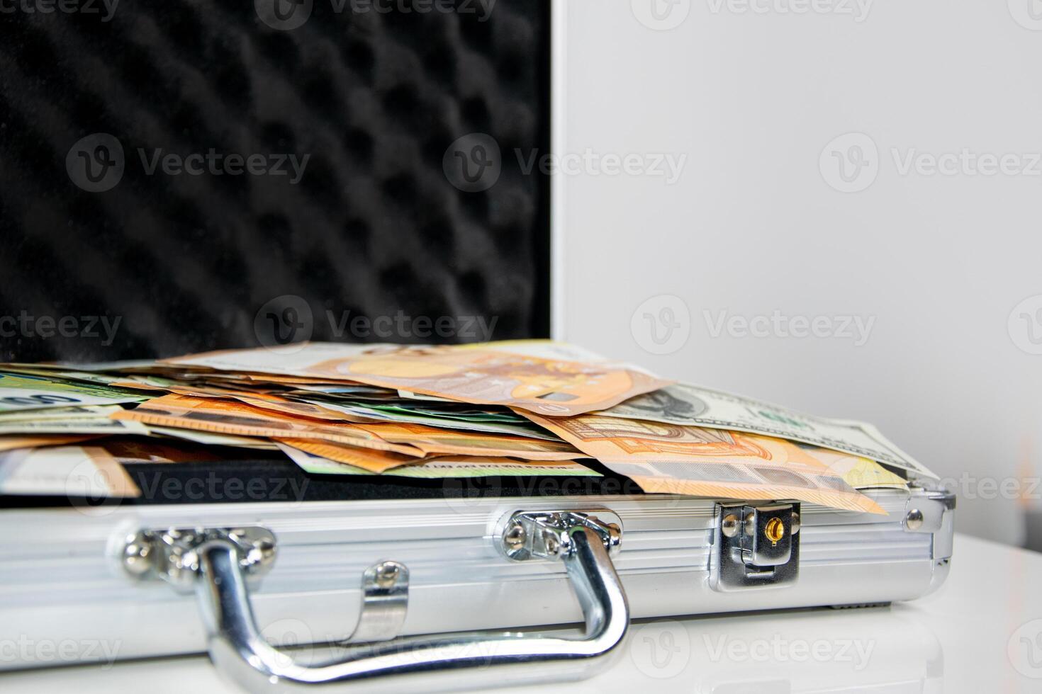 A close-up shot of a silver briefcase lying open on a white surface, revealing stacks of Euro bills inside photo