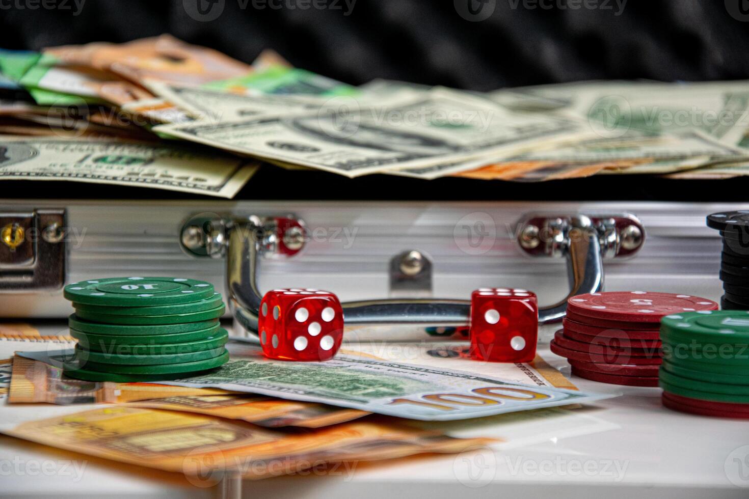 Close-up of red dice and stacks of poker chips on a white surface. A silver suitcase filled with money is visible in the background photo