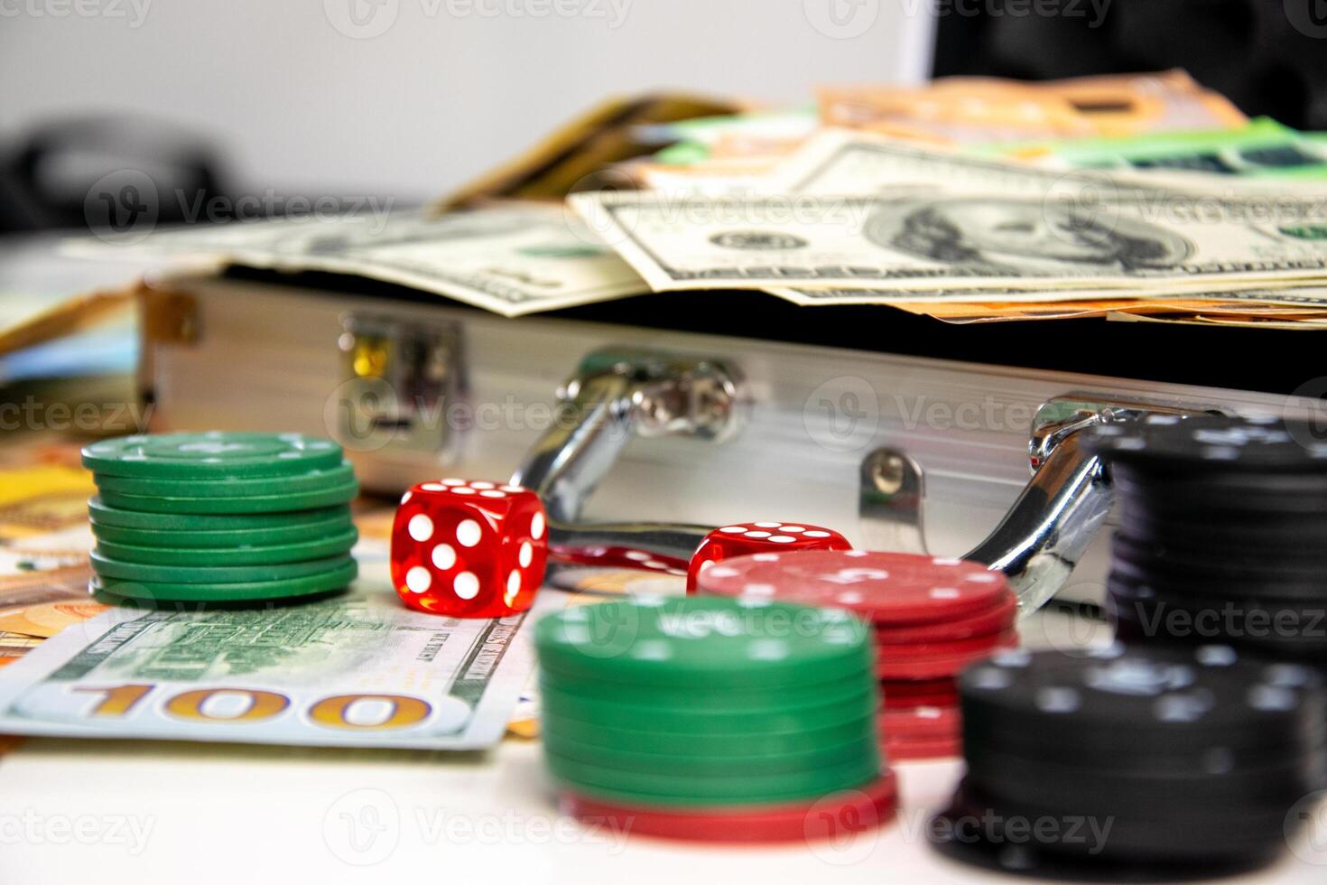 A close-up shot of a silver briefcase with red dice and stacks of casino chips and cash spilling out photo