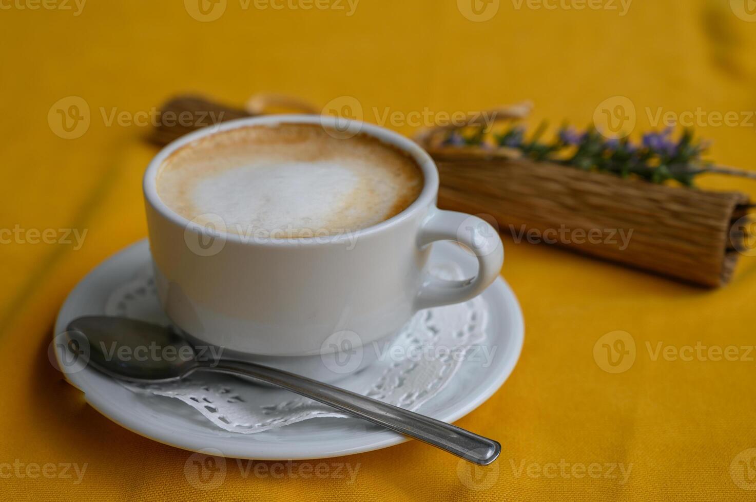 Warm coffee cup on a vibrant yellow tablecloth with a touch of nature beside it photo
