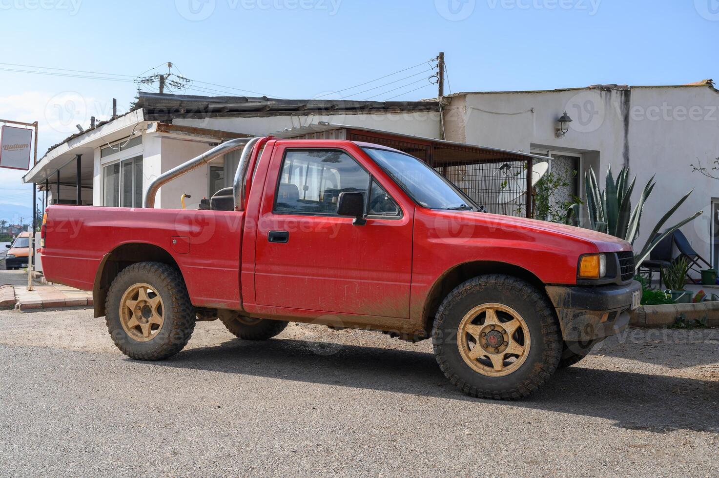 Red pickup truck parked in a dusty street near a rustic building under a clear blue sky photo