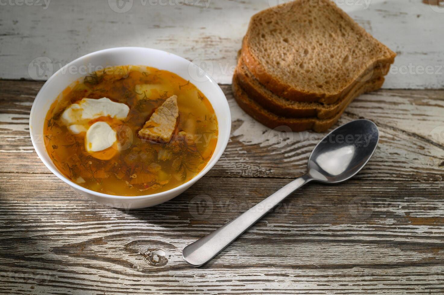 Warm bowl of hearty soup served with sliced brown bread on a rustic wooden table photo