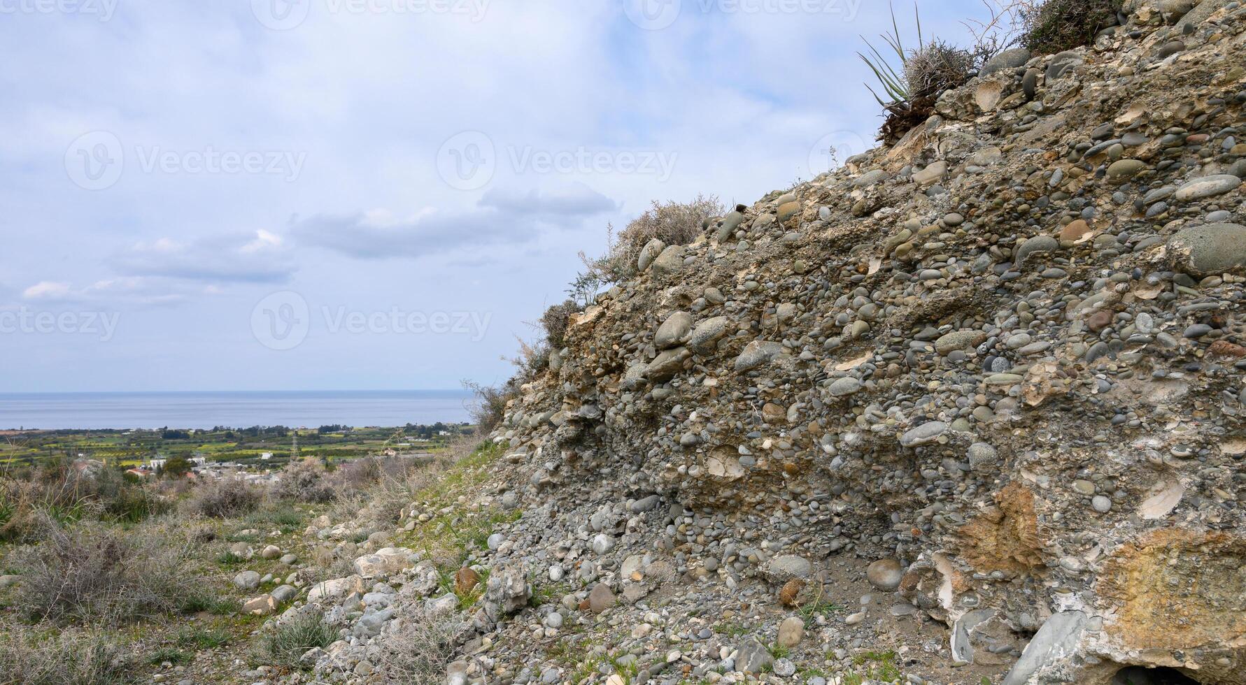 Unique geological formation reveals stones and soil against a beautiful coastal backdrop in daylight photo