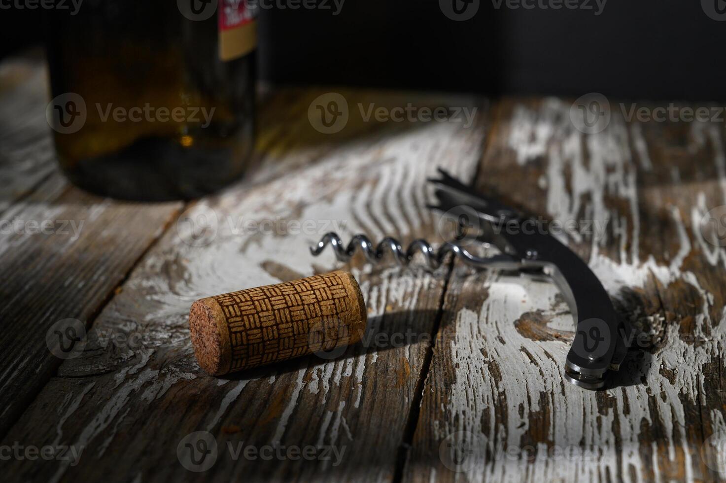 Corkscrew and cork resting on rustic wooden table with a bottle in the background at evening light photo
