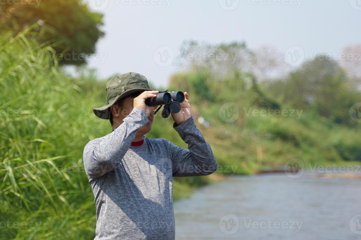 Asian man uses binoculars to observe local birds along a river. photo