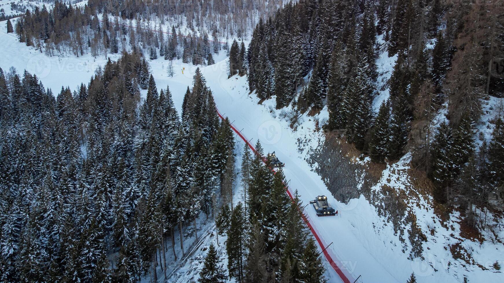 Two snowcats preparing ski slopes. Aerial view of the two vehicles between trees in the mountains in winter landscape photo