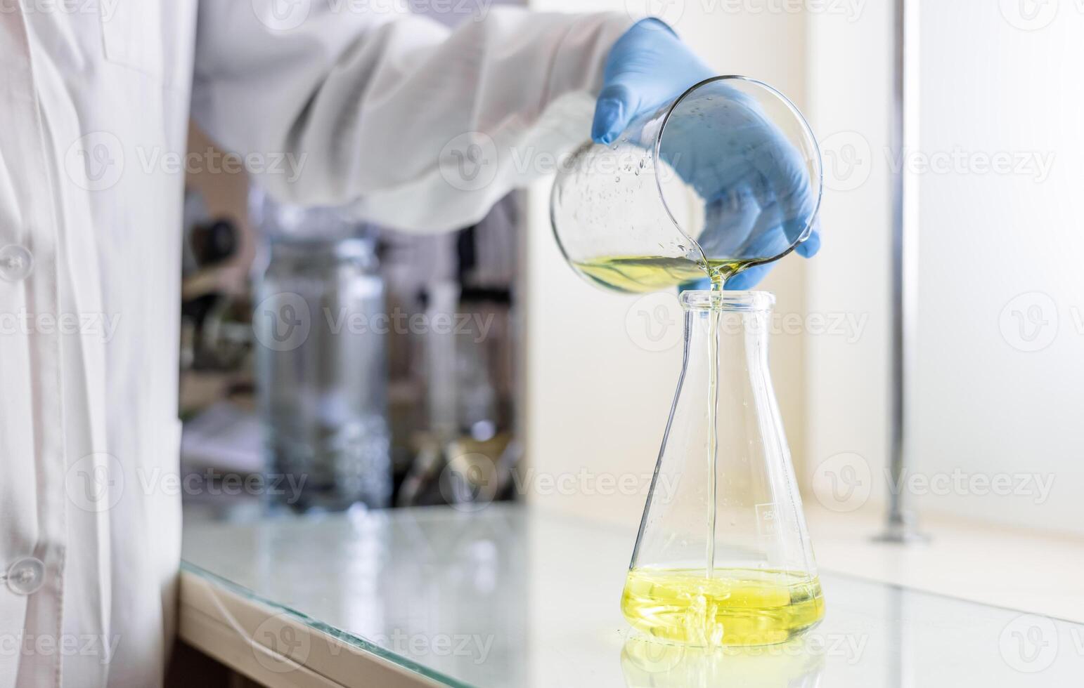 A person in a lab coat pouring yellow liquid into a beaker photo