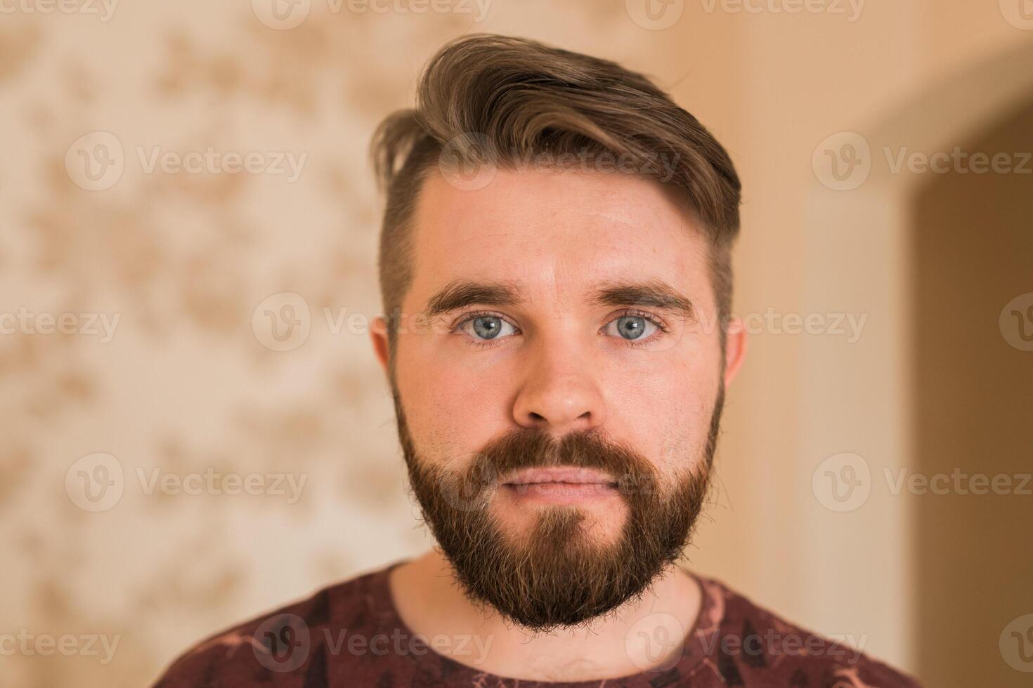 Portrait of an attractive young bearded hipster man looking at the camera standing in modern house, wearing a casual shirt. The view while the calling concept, call portrait photo