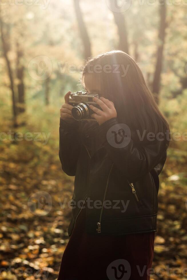 Child girl using an old-fashioned camera in autumn nature. Photographer, fall season and leisure concept. photo