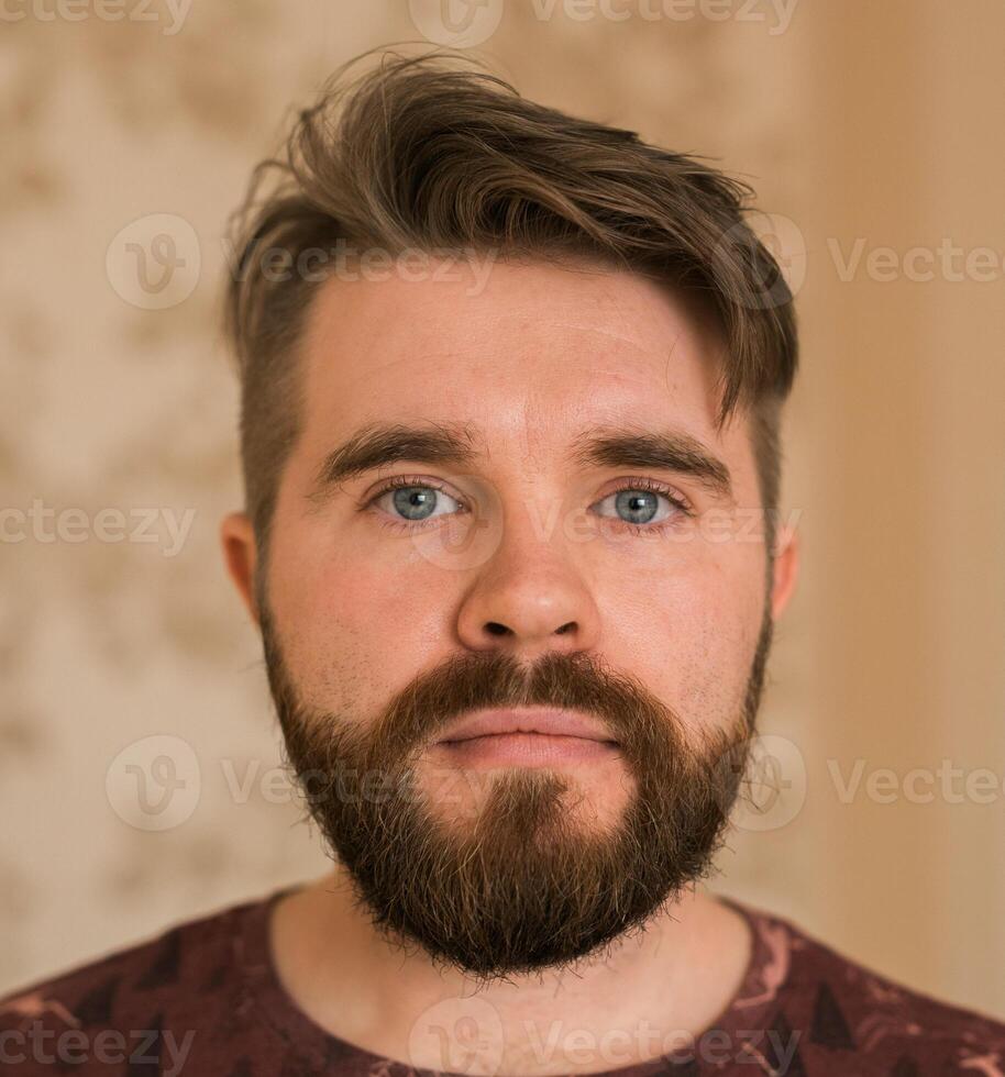 Portrait of an attractive young bearded hipster man looking at the camera standing in modern house, wearing a casual shirt. The view while the calling concept, call portrait photo