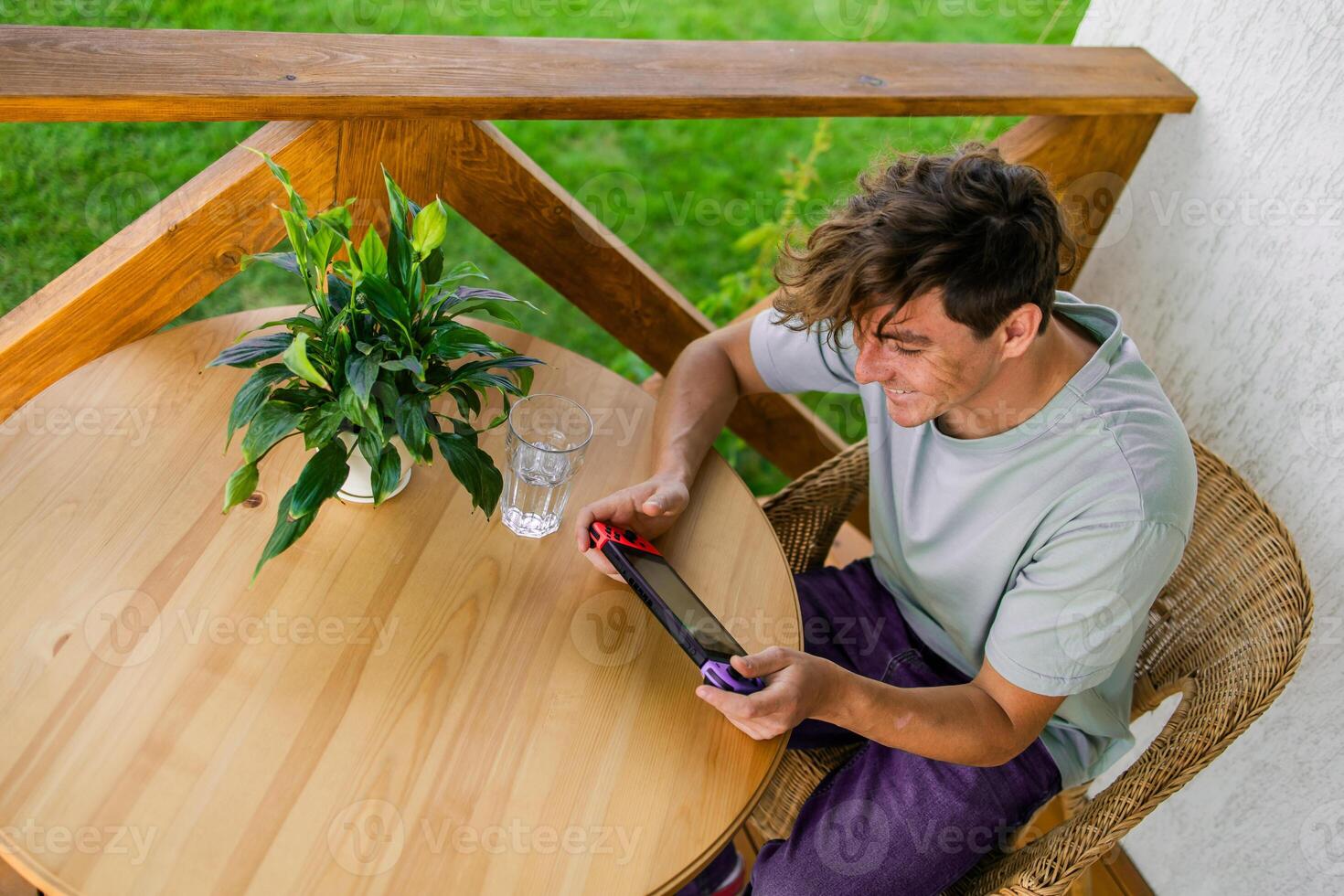 Young man playing game drinking water at terrace in summer day. Technology and game addiction concept photo