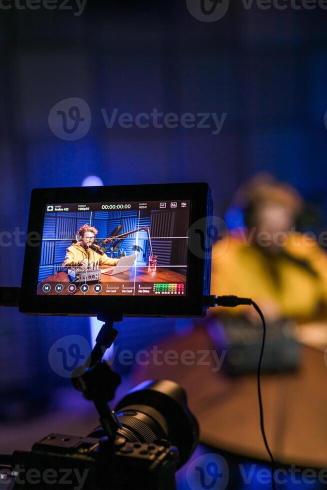 Cheerful young man recording podcast in studio. Confident man with headphones and microphone recording a podcast. Happy guy talking on web radio. photo