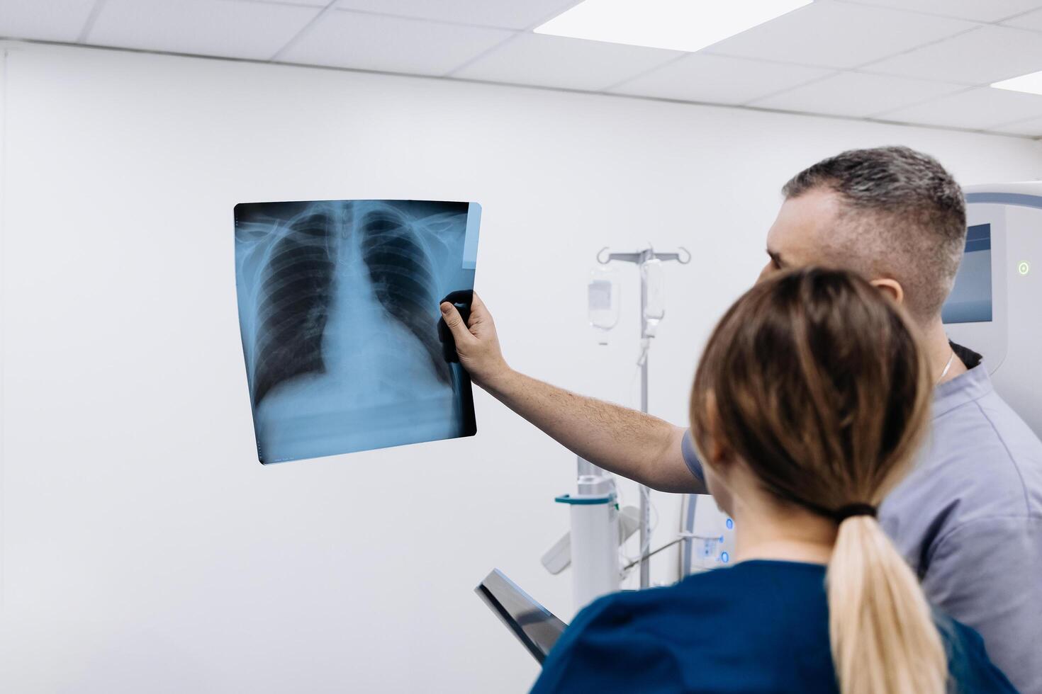 Two doctors watching x-ray image in a hospital. Lung disease. Doctor examining chest x-ray against white MRI room background. CT scan in a modern diagnostic center. Check-up, radiology, ads photo