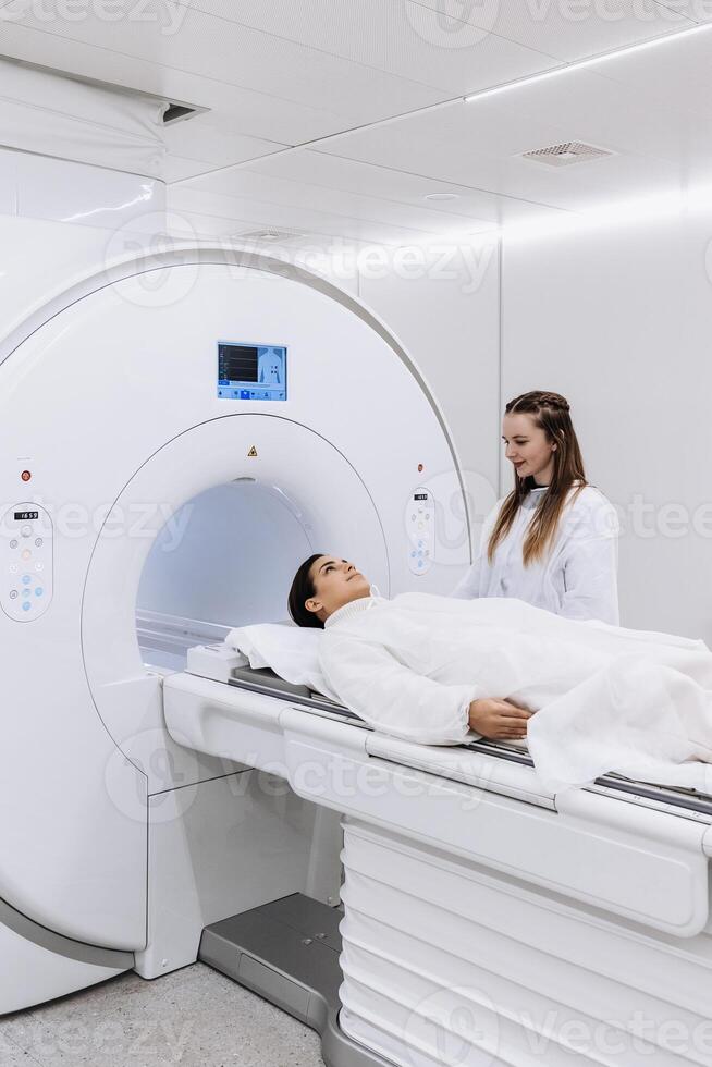 Female doctor is preparing patient for magnetic resonance procedure. Patient is lying at CT scanner bad and waiting to be scanned. Medical Lab with High-Tech Equipment. Vertical shot photo