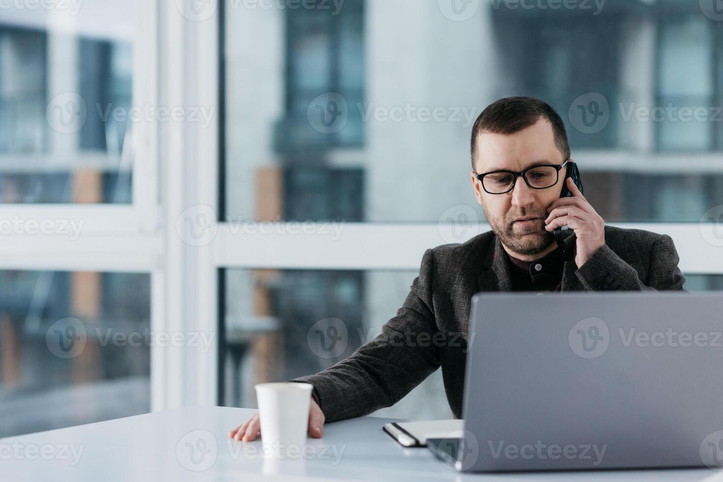 Middle aged caucasian business manager ceo using cell phone mobile app, laptop. Focused mature man businessman holding smartphone sit in office working online on gadget with copy space. photo
