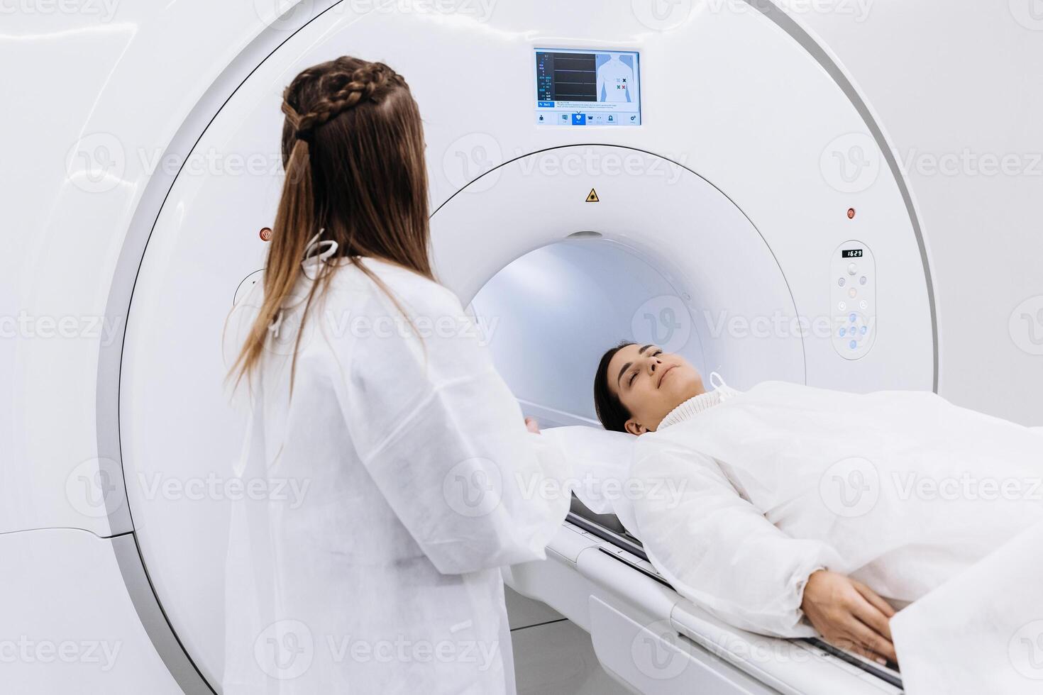 Female doctor is preparing patient for magnetic resonance procedure. Patient is lying at CT scanner bad and waiting to be scanned. Medical Lab with High-Tech Equipment. Medicine advertising photo