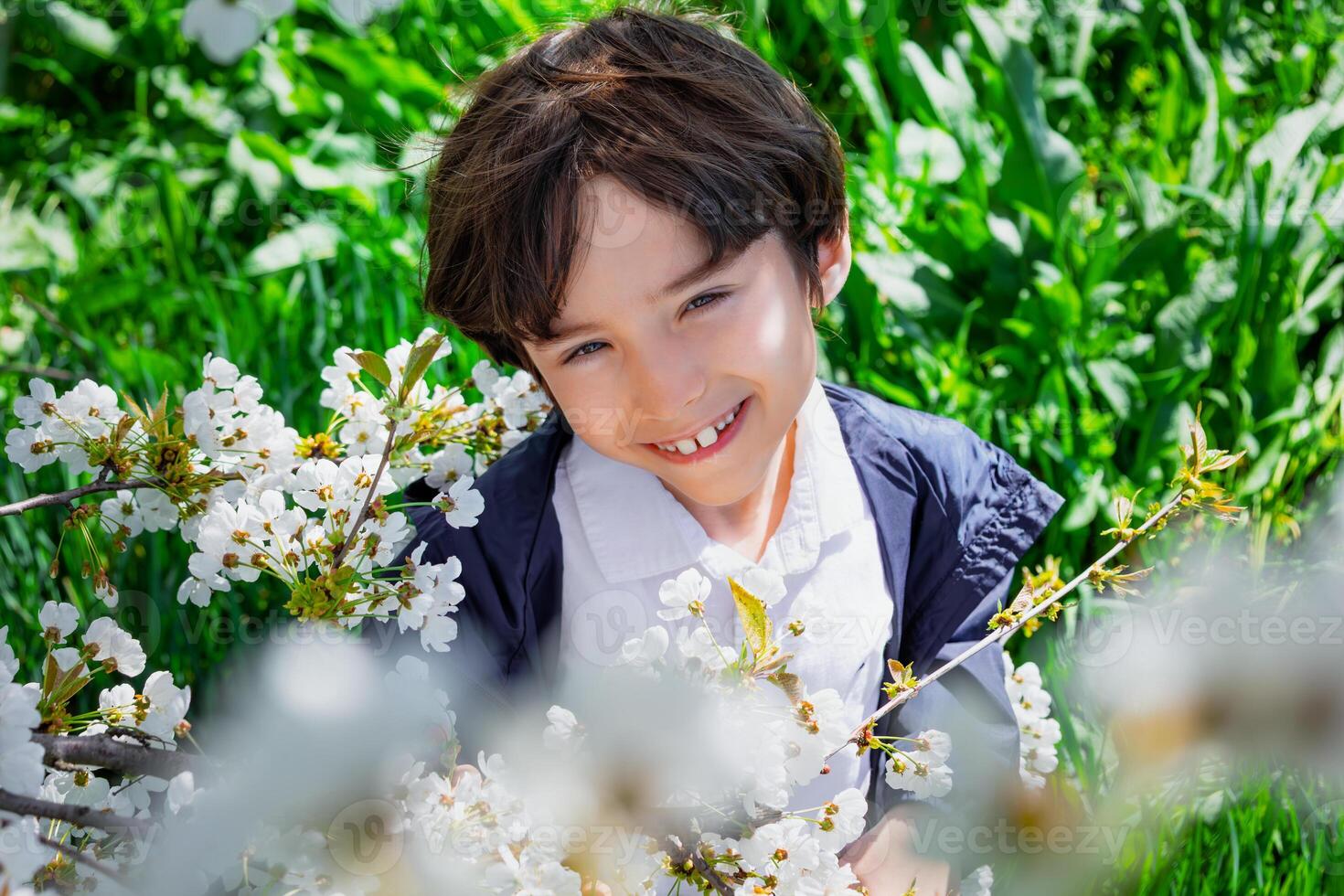 Smiling boy in white shirt among blooming branches on a sunny spring day. Childhood happiness and nature connection photo