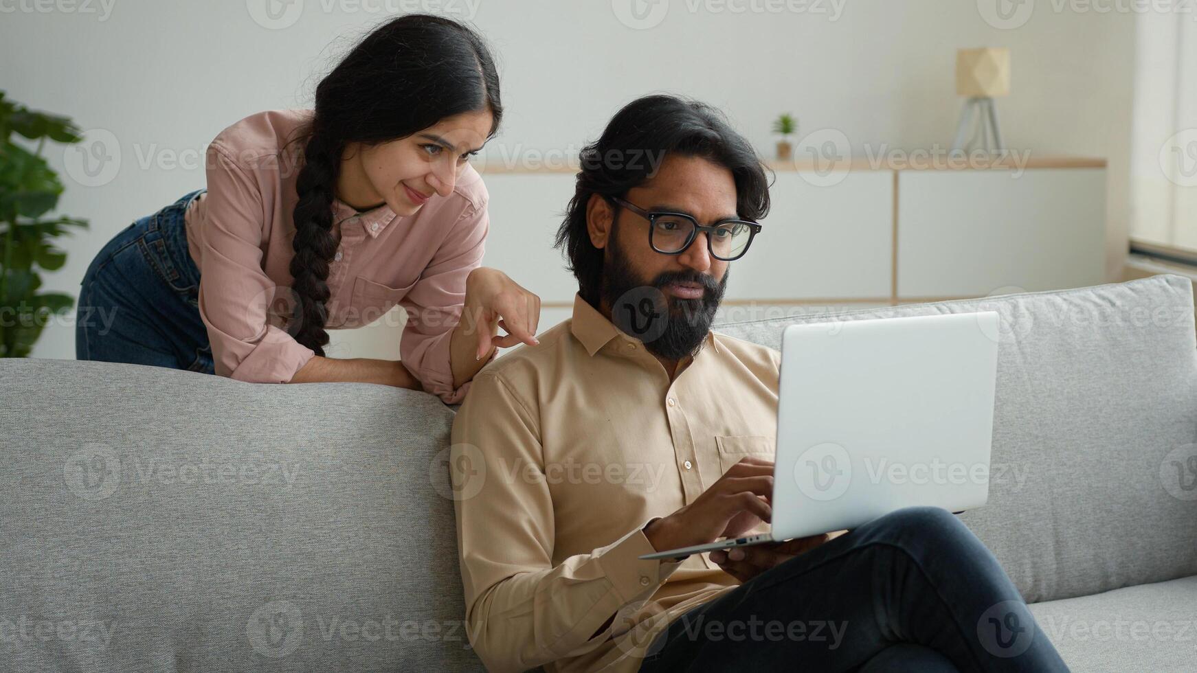 Arabian Indian couple on couch sofa use computer laptop shopping online internet store happy multiracial wife husband smiling lovely customers woman and man search goods purchase on website at home photo