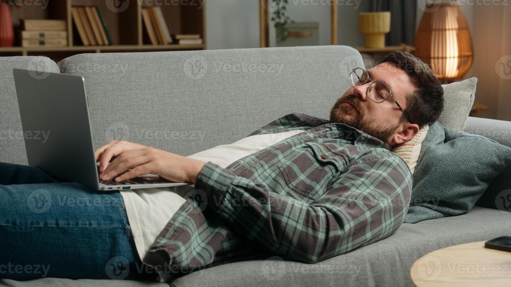 Lazy relaxing lying on sofa couch Caucasian man male freelancer businessman business guy online shopping order food delivery laptop computer working pc browsing net playing internet game web at home photo
