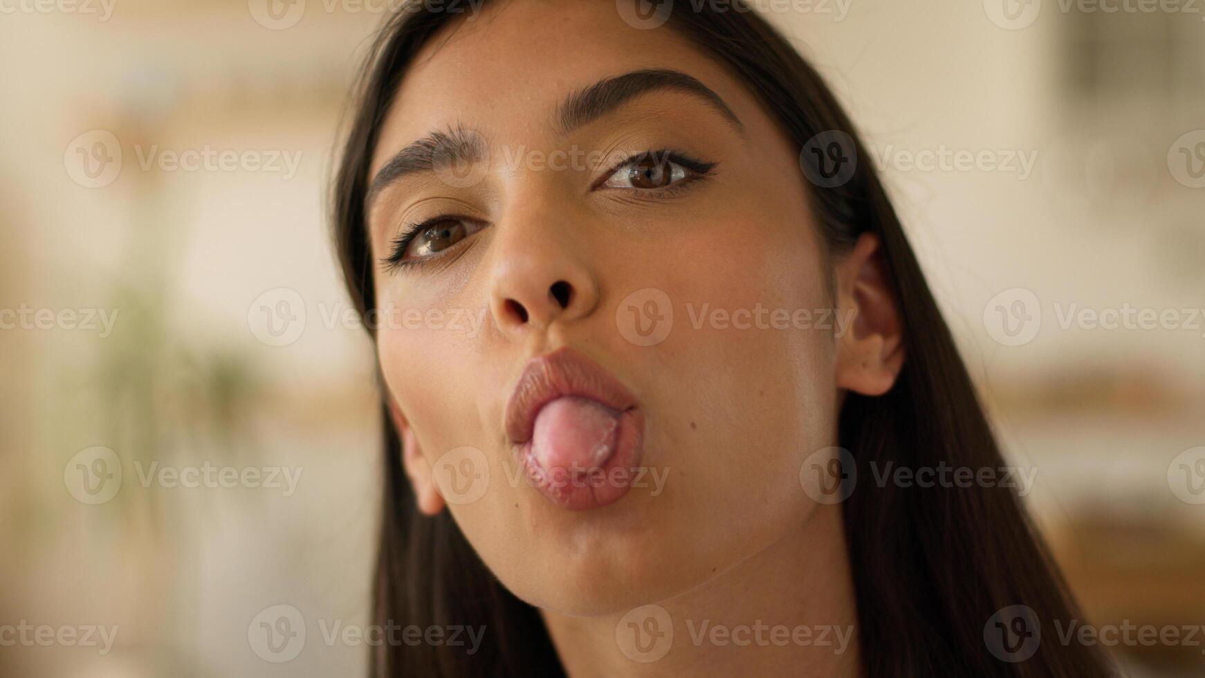Happy smiling positive funny playful Arabian woman Indian girl female Hispanic lady smiling attractive pretty at home indoors playing grimace showing tongue having fun joyful humorous grimacing face photo