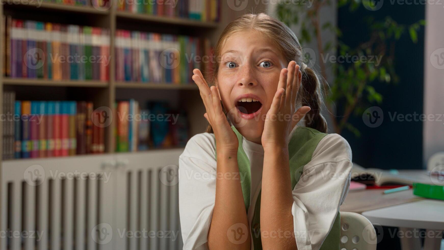 Overjoyed shocked surprised Caucasian little girl child kid schoolgirl schoolchild pupil student learner looking at camera screaming yelling wow shouting shock surprise indoor school library education photo