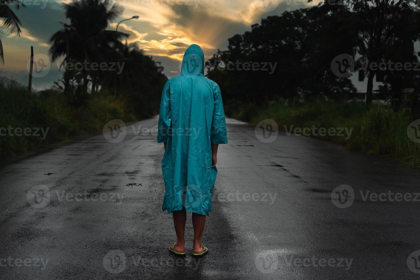 Depressive concept with lonely man in raincoat standing on wet road under rain in sunset photo