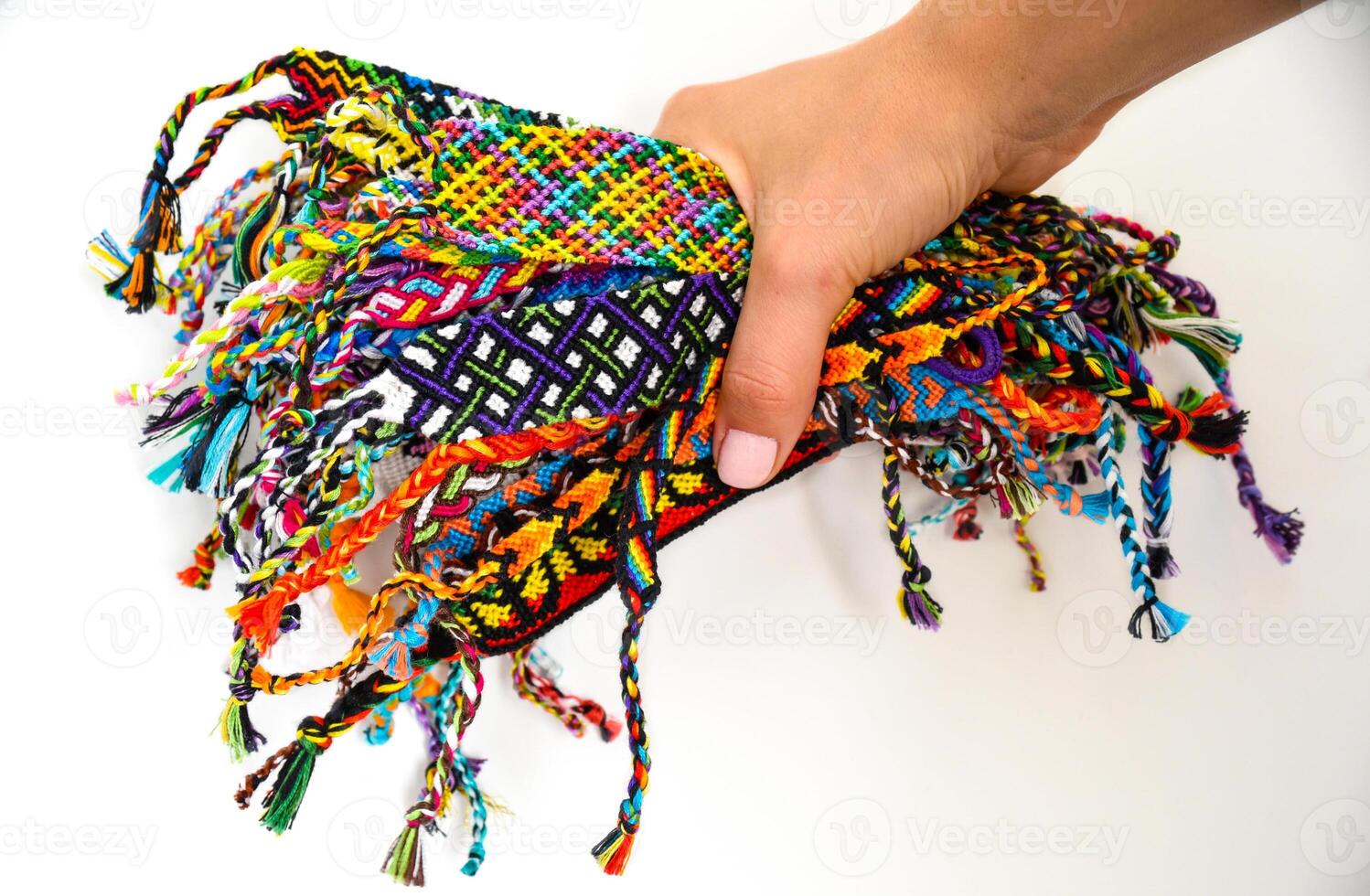 hand holding many woven multi-colored DIY friendship bracelets handmade of embroidery thread with knots on white background. photo