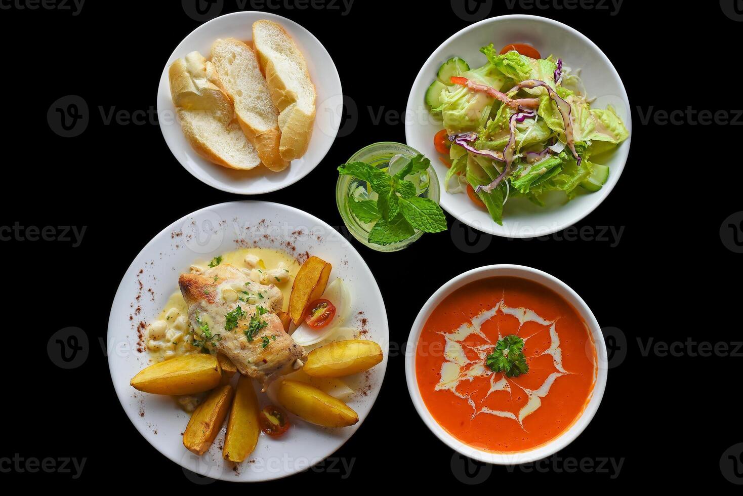 Lunch set made of tomato cream soup salad chicken with potato, lemonade on black background photo
