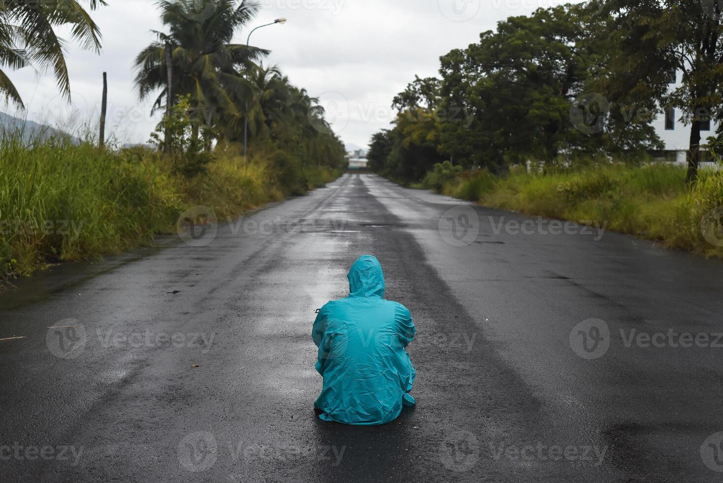 Depressive concept with lonely man in raincoat sitting on wet road under rain photo