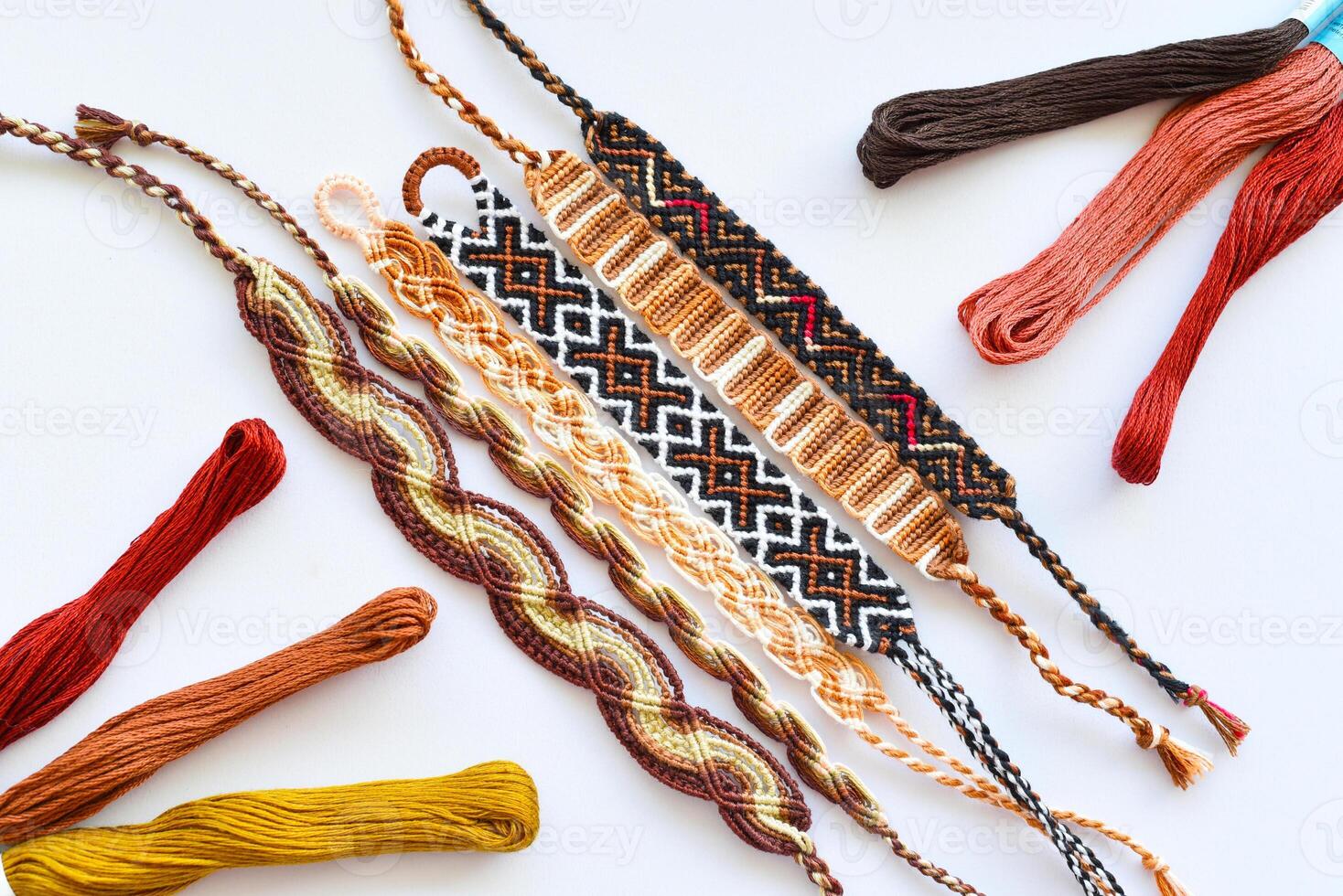 Woven DIY friendship bracelet with brown patterns next to skeins of embroidery floss photo