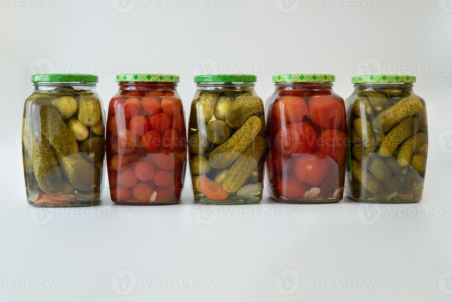 several glass jars of canned cucumbers, gherkins and tomatoes photo