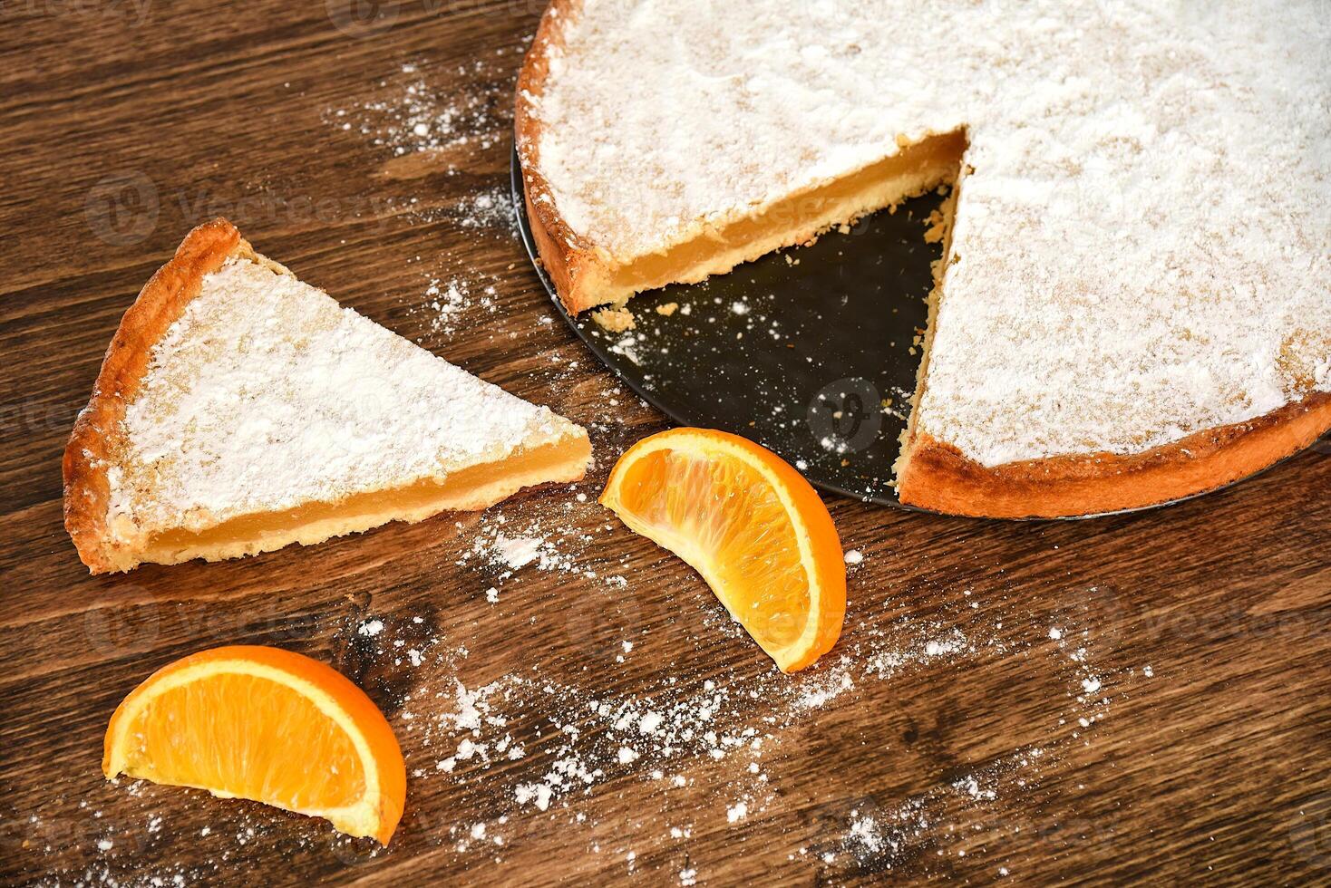 Piece of homemade pie with lemon and orange filling, covered with powdered sugar on a wooden table photo