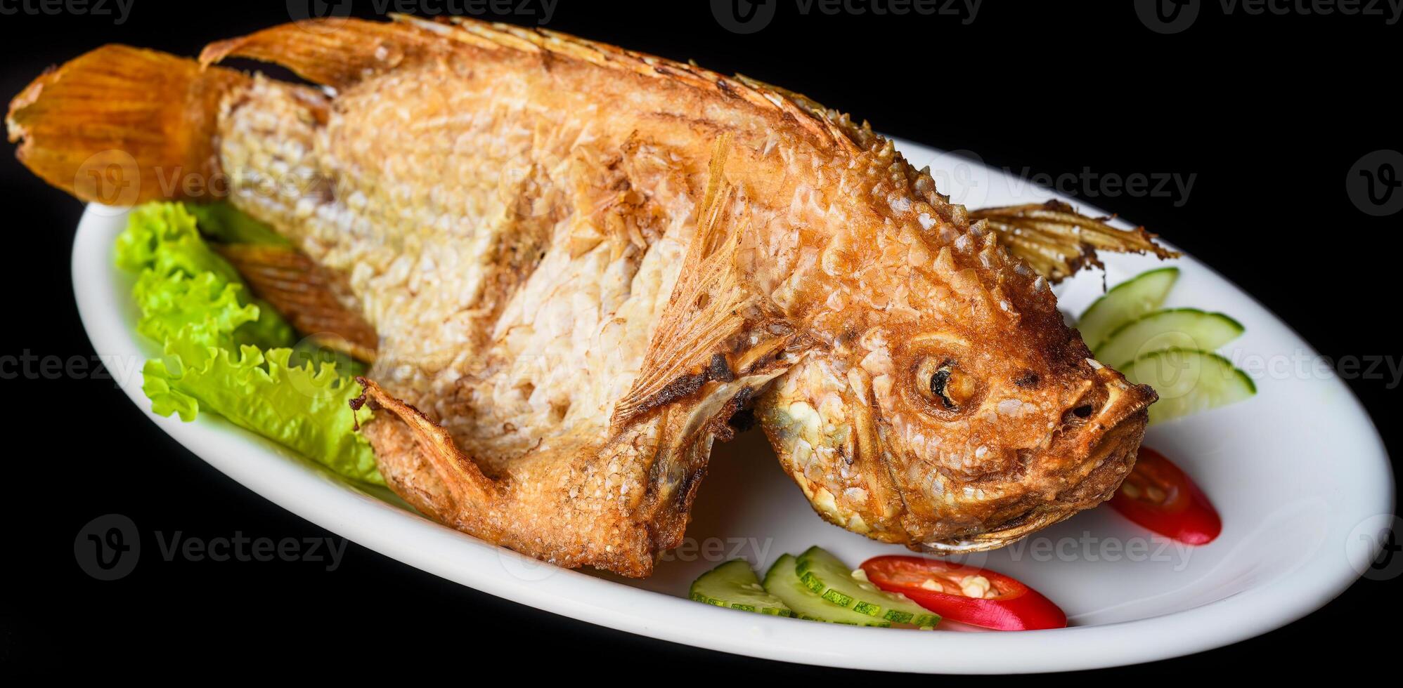 Fish grilled in batter with vegetable and greens on white plate isolated on black background side view photo