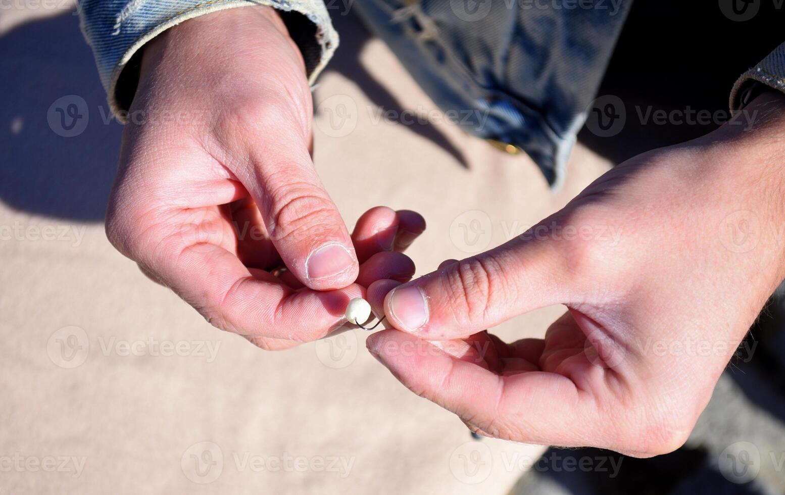 Fishing metall hook with fishing bait corn with garlic, in the form of a ball. Male hands sticking this bait against beige background photo