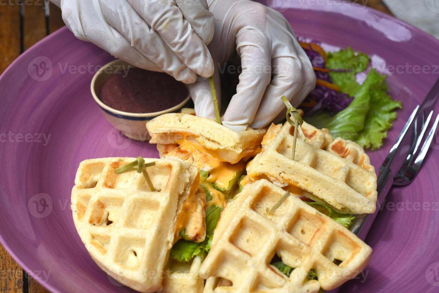 Hands in rubber gloves serving Belgium waffles with pan fried chicken on purple plate closeup photo