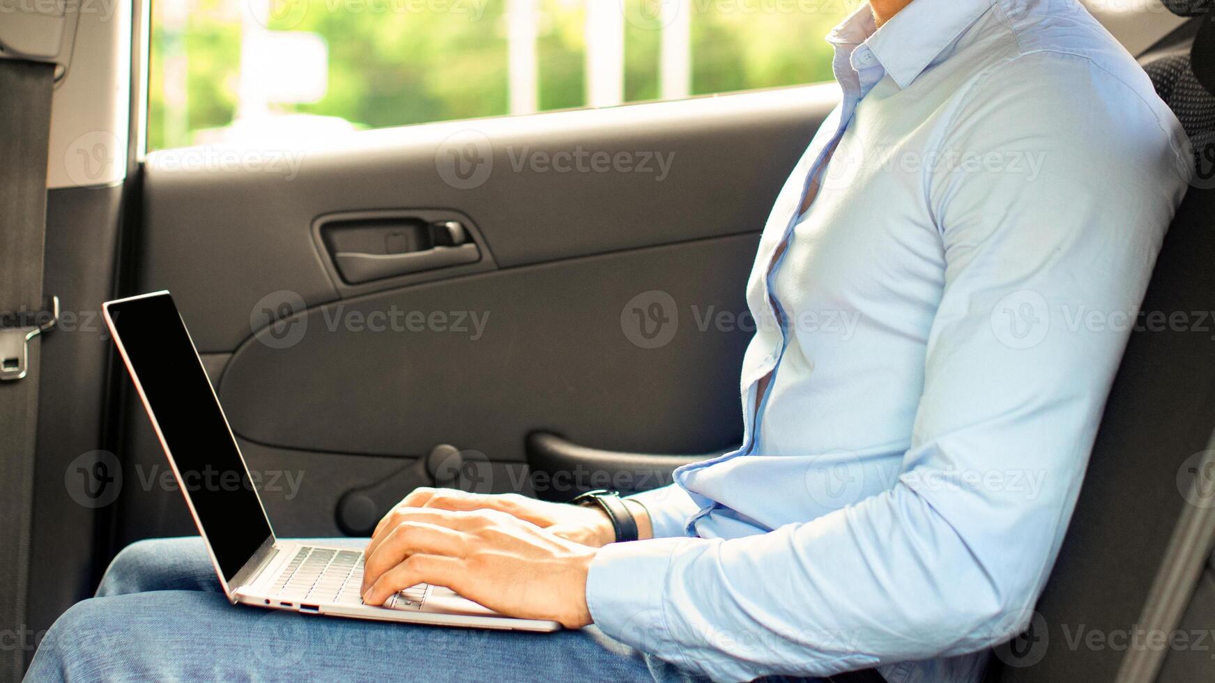 Handsome arabic guy in formal outfit entrepreneur sitting at auto back seat, using laptop with blank screen, typing on keyboard, sending emails while going to business meeting, mockup, copy space photo