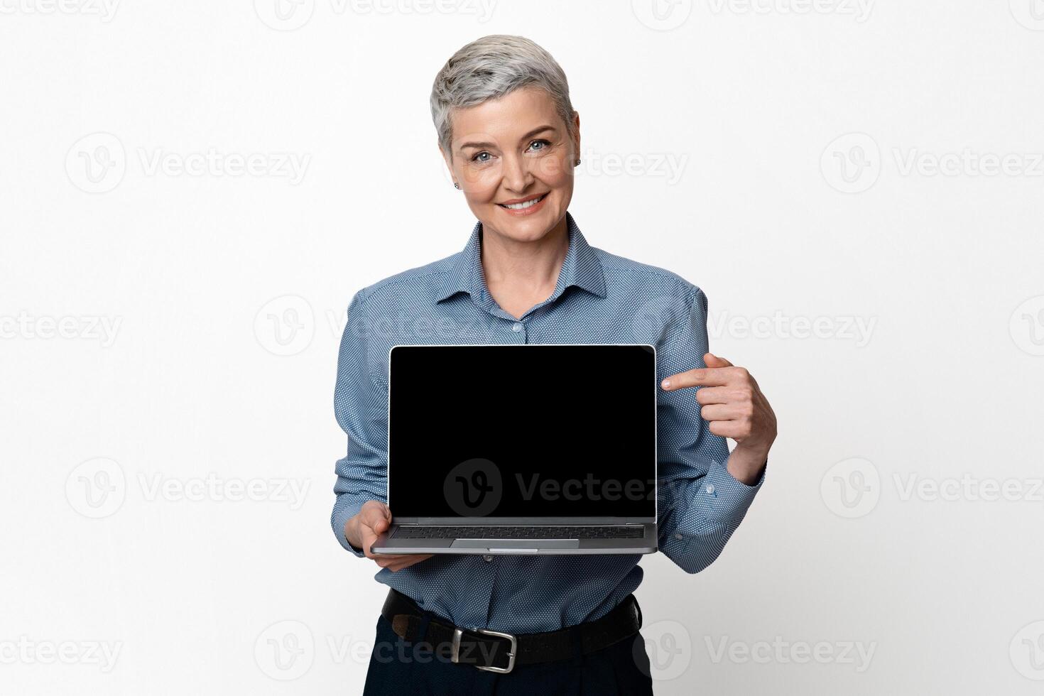 Business Platform. Smiling Middle Aged Woman Holding And Pointing At Laptop Computer With Blank Black Screen For Mockup, Light Background photo