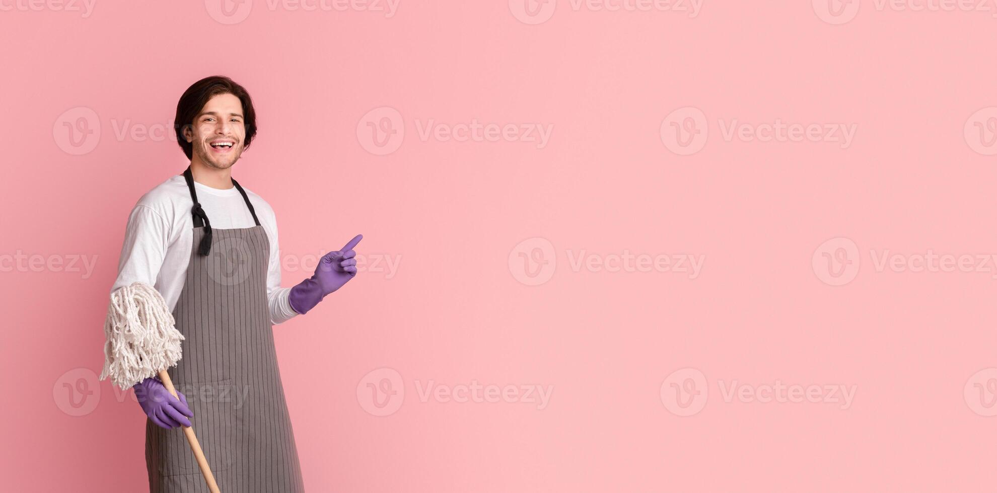 Cleaning Concept. Smiling man in apron holding mop and pointing at copy space on pink background, panorama photo