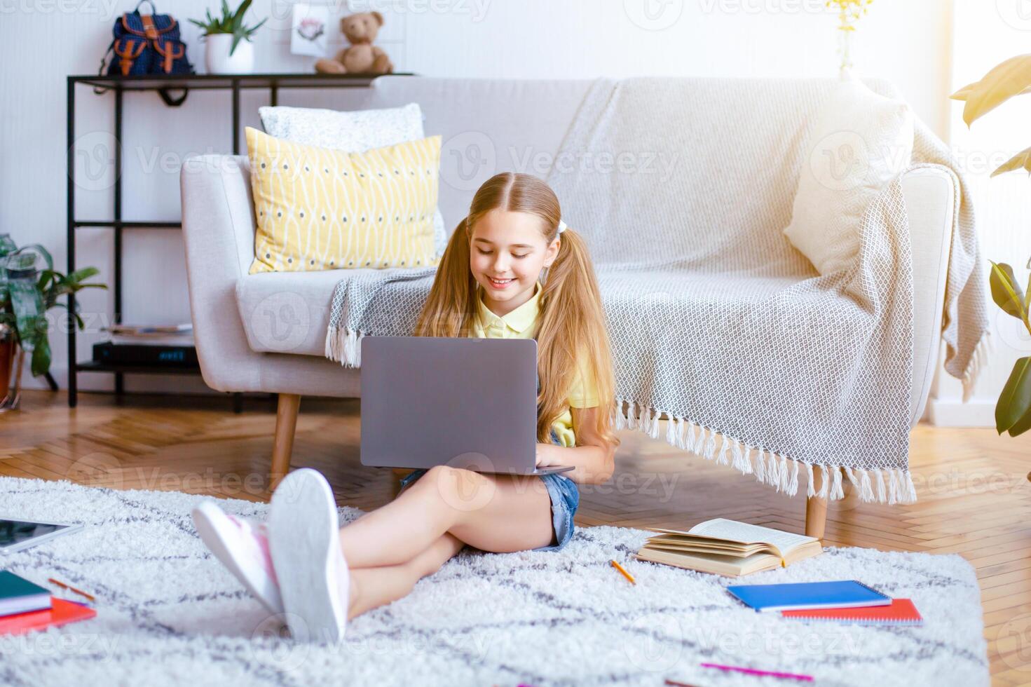 Modern Technology Concept. Full length portrait of happy teenage girl resting and sitting on the floor carpet, leaning on sofa, using her laptop, typing on keyboard, chatting or browsing web photo