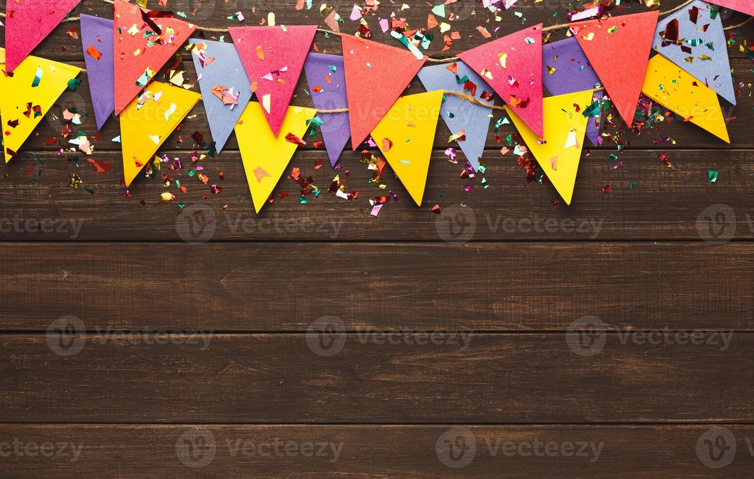 Border of colorful paper flags garland and confetti on rustic wood. Birthday party decoration background, top view, copy space. Mockup for greeting card photo