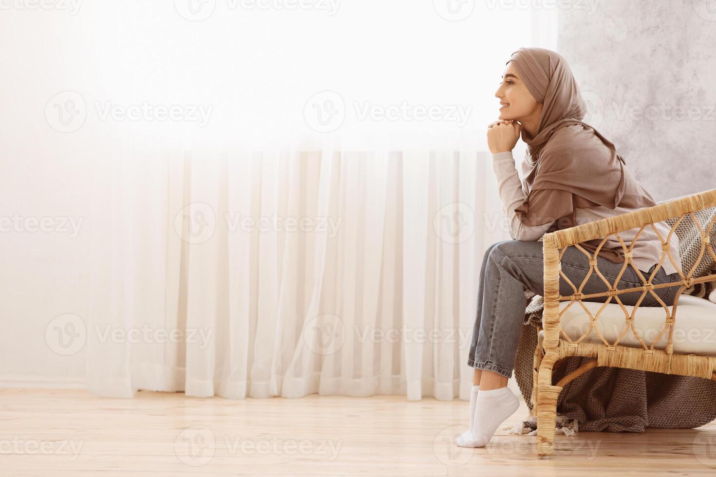 Side View Portrait Of Pensive Arabic Woman In Hijab Relaxing In Wicker Chair, Looking Away, Thinking About Something, Enjoying Weekend, Copy Space photo