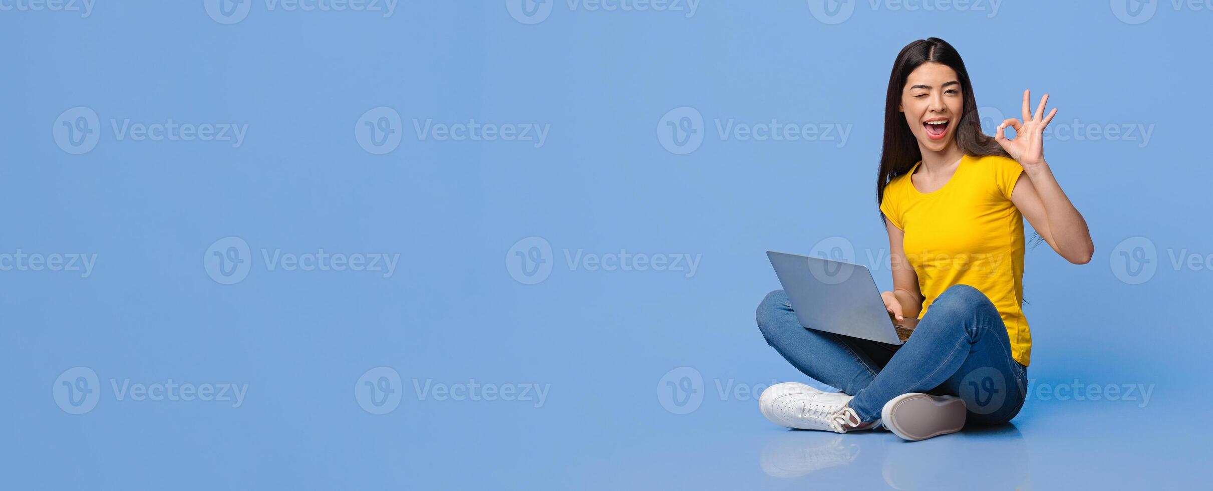 Freelance Jobs For Young People. Positive asian girl sitting with laptop on laps and showing ok sign over purple studio background, panorama photo