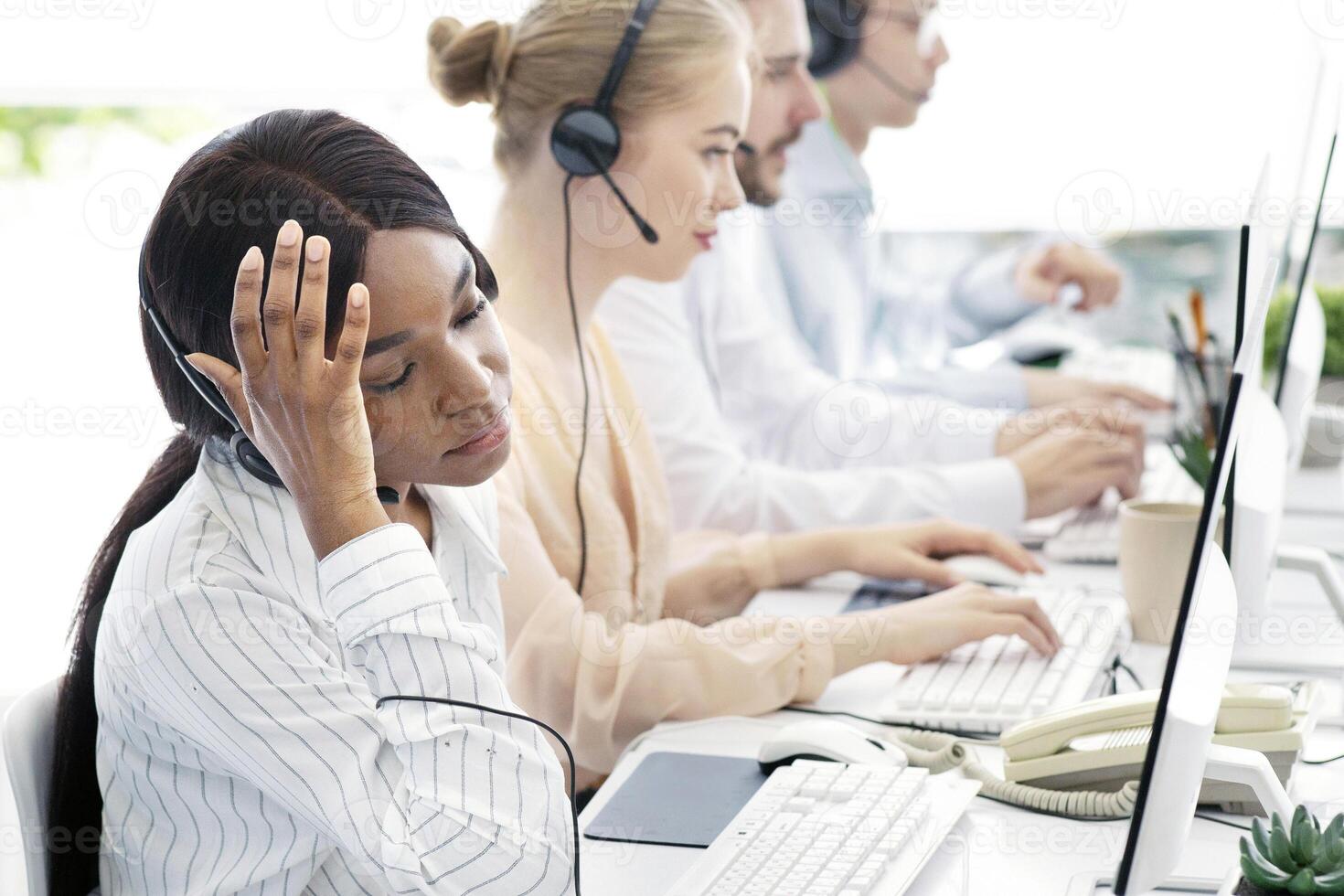 African American female helpline operator feeling exhausted after talking to clients at call centre, copy space. Overworked technical support assistant dealing with workplace stress at office photo