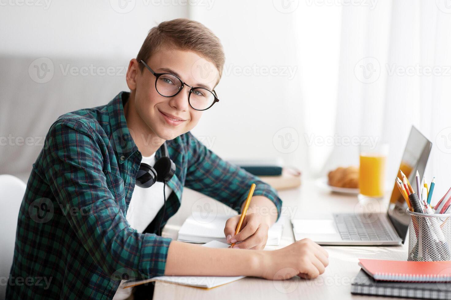 Happy teen guy doing homework at home, side view, empty space photo
